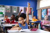 African american girl raising her hands while sitting on her desk in the class at school