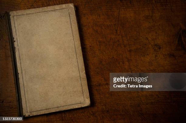 old book with blank cover resting on old wooden desk top - blank book on desk stock-fotos und bilder