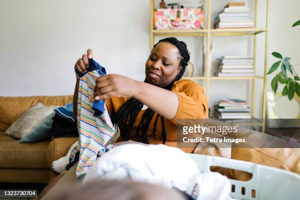 woman sitting on sofa and folding laundry - laundry woman stock pictures, royalty-free photos & images