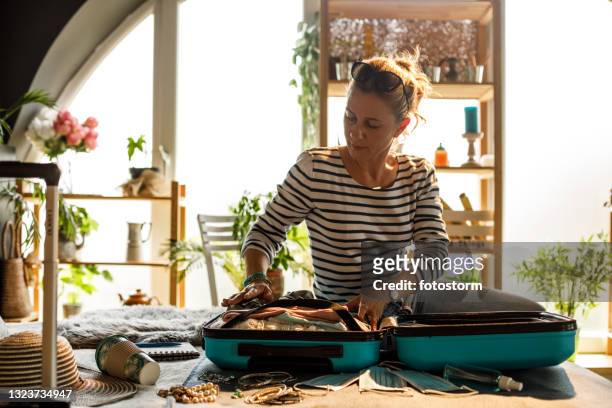woman sitting on her bed and packing a suitcase for a vacation - woman packing suitcase stock pictures, royalty-free photos & images