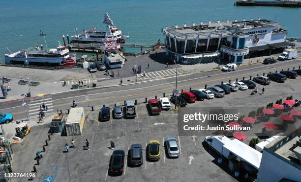 In an aerial view, cars and tables fill a parking lot next to a restaurant and bay cruise terminal at San Francisco's Fisherman's Wharf tourist...