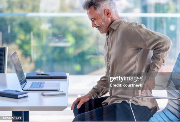 mature business man with holding his back in pain. - man office chair stock pictures, royalty-free photos & images