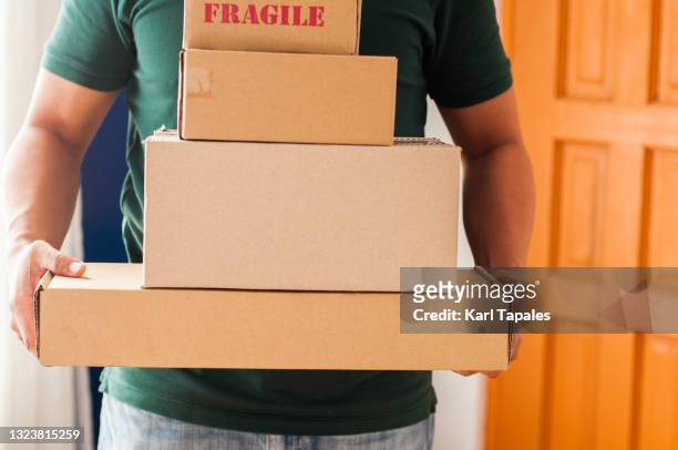 front view of southeast asian man holding stacks of carton packages indoor - rinviare la palla foto e immagini stock