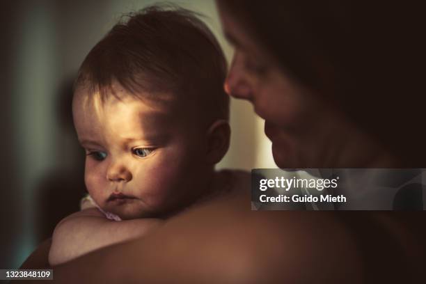 mother hugging her tired baby girl in sunlight. - dark baby stock pictures, royalty-free photos & images