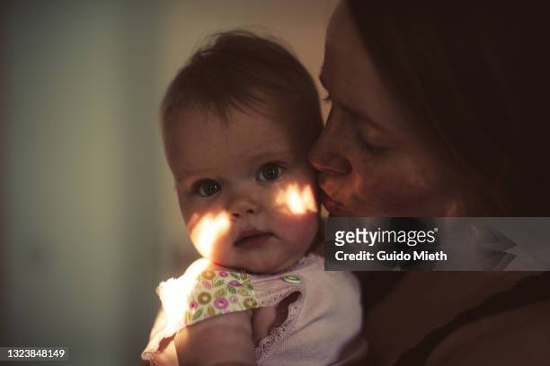 happy mother kissing her smiling baby girl at home. - dark baby stock pictures, royalty-free photos & images