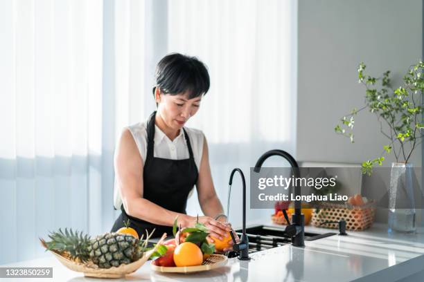 an asian woman washes fruit in her kitchen - food waste stockfoto's en -beelden