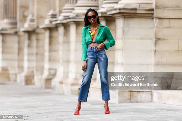 Emilie Joseph @in_fashionwetrust wears black sunglasses, diamond earrings, a V-neck emerald green crop top with knot, a yellow shellfish necklace...