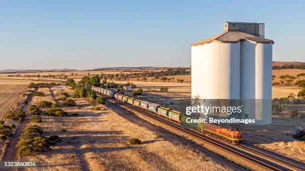 aerial view, loaded grain train with old locomotives passing silo at sunset - silage stock pictures, royalty-free photos & images