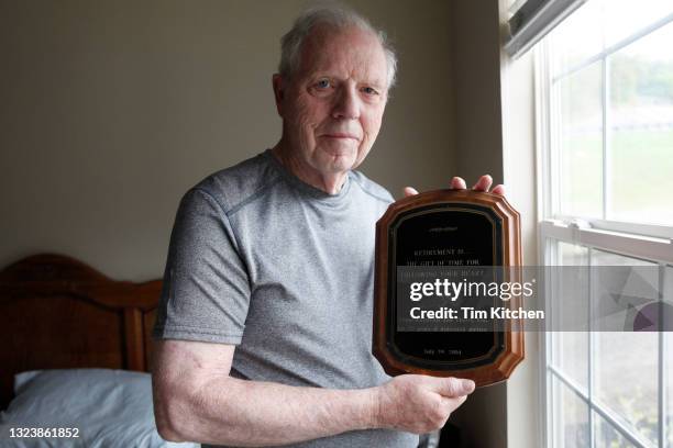 portrait of senior man near window, holding an award plaque, smiling at camera - targa premio foto e immagini stock