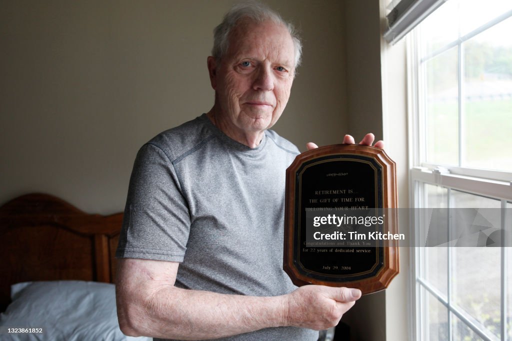 Portrait of senior man near window, holding an award plaque, smiling at camera