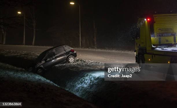 rescue worker helping car after sliding into a ditch on a snowy road at nighttime - ditch stock pictures, royalty-free photos & images