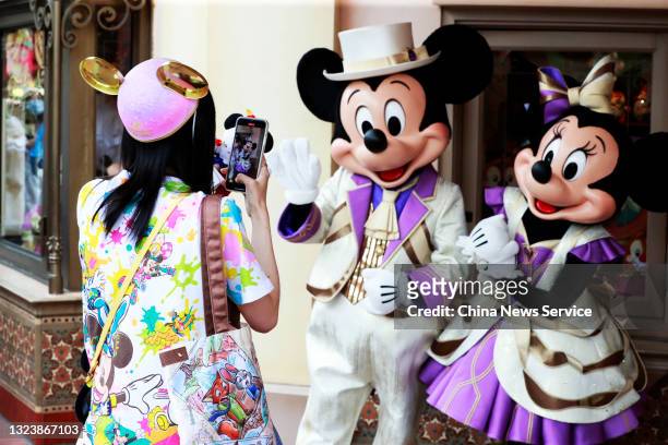 Tourist takes photos of cast members dressed as Mickey and Minnie Mouse at Shanghai Disneyland theme park during the resort's 5th anniversary...