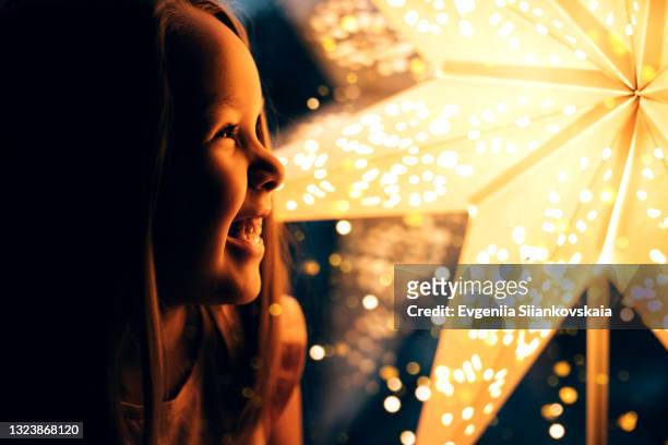 close-up portrait of little cute girl against the christmas lamp in playroom at home. - young child light stock pictures, royalty-free photos & images