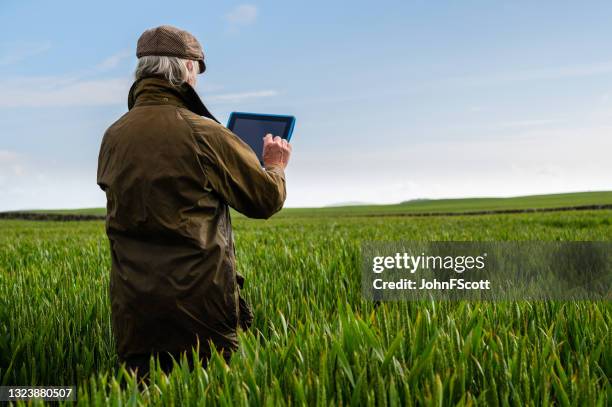 senior man using a digital tablet in a field - waxed jacket stock pictures, royalty-free photos & images