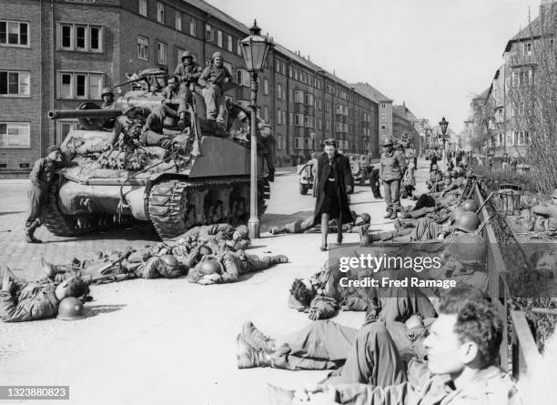 Lone German civilian woman passes a M-4 Sherman tank and infantrymen of the US 11th Armoured Division, United States 9th Army as they relax and sleep...