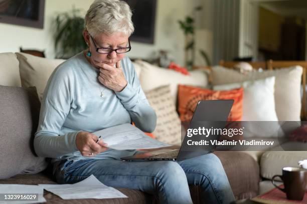 with her hand on her chin, a mature lady puzzles at her monthly finances - grounds stock pictures, royalty-free photos & images