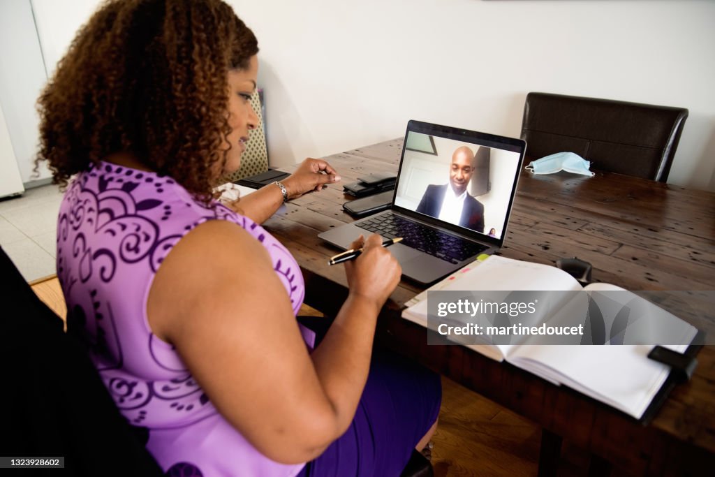 Reife afroamerikanische Frau arbeitet von zu Hause aus in Telefonkonferenz.