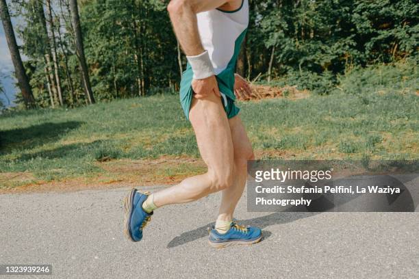 middle age man running on the side of a asphalted mountain road - hip pain stock-fotos und bilder
