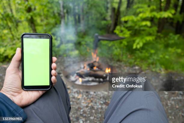 close-up of man hands reading on chroma key green screen mobile phone by the campfire - mature man using phone tablet stock pictures, royalty-free photos & images