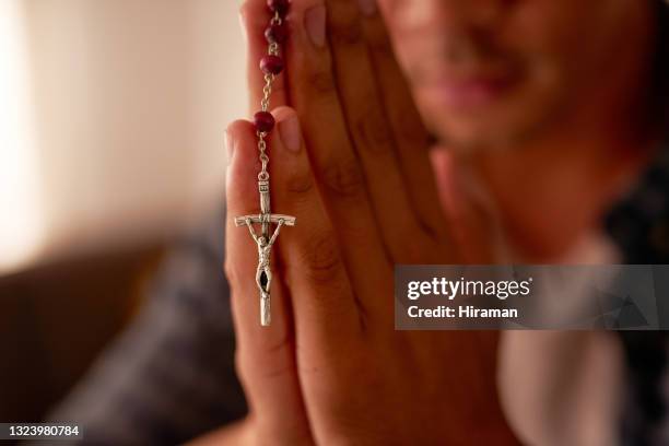 foto recortada de un hombre irreconocible sentado solo en casa y usando su rosario durante la oración - rosary beads fotografías e imágenes de stock