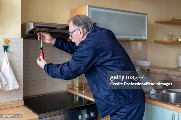 o homem mais velho está trabalhando na cozinha e consertando o filtro extrator. - tighten - fotografias e filmes do acervo