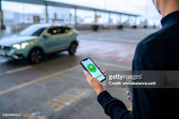 chic joven asiático utilizando el dispositivo de aplicación móvil en el teléfono inteligente para pedir un servicio de recogida de taxis por la carretera urbana en la calle del centro de la ciudad. servicio rápido y confiable. carsharing y temas de ne - car rental fotografías e imágenes de stock