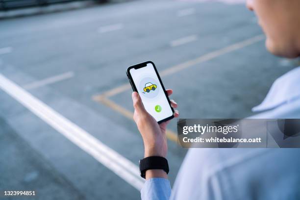 young asian man ordering a taxi with mobile app on smartphone, waiting for taxi in downtown city street. technology and transportation in everyday life - car pooling stock pictures, royalty-free photos & images