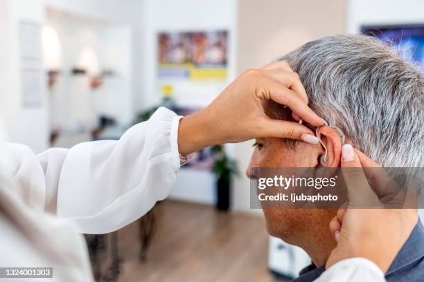female doctor fitting a male patient with a hearing aid - ear exam stock pictures, royalty-free photos & images