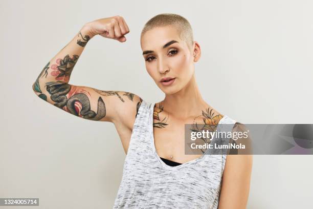 retrato de una atractiva joven flexionando su brazo sobre un fondo gris - female body piercing fotografías e imágenes de stock