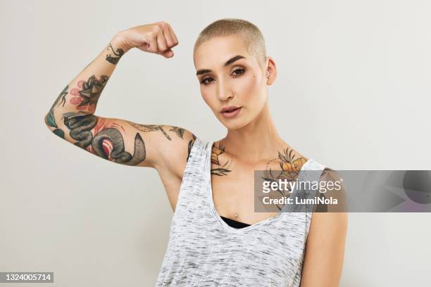 portrait of an attractive young woman flexing her arm against a grey background - tattoo arm stockfoto's en -beelden