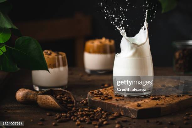 milk splash in glass with coffee beans on table - coffee splash stockfoto's en -beelden