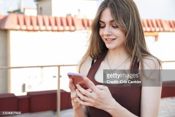 beautiful teenager girl using smartphone in terrace - cris cantón photography stock-fotos und bilder
