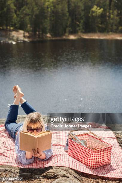 woman lying on picnic blanket and reading book - summer picnic stockfoto's en -beelden