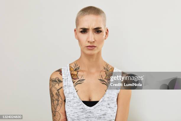 portrait of an angry young woman displaying her tattoos against a grey background - frowning stock pictures, royalty-free photos & images