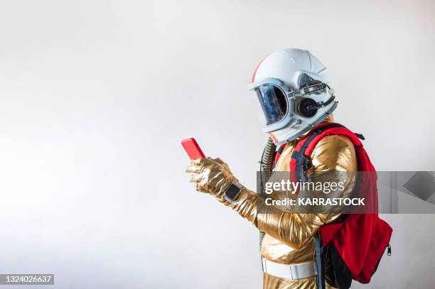 man dressed as an astronaut with backpack holding a smartphone. - gold suit fotografías e imágenes de stock