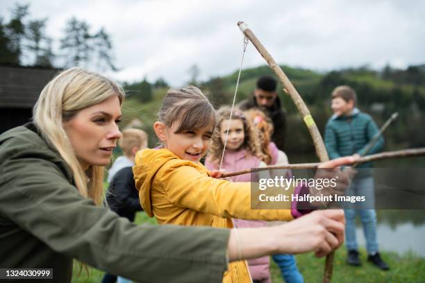 teacher helping schoolgirl to shoot from bow and arrow in nature, learning and exploring outdoors. - bow and arrow stock pictures, royalty-free photos & images