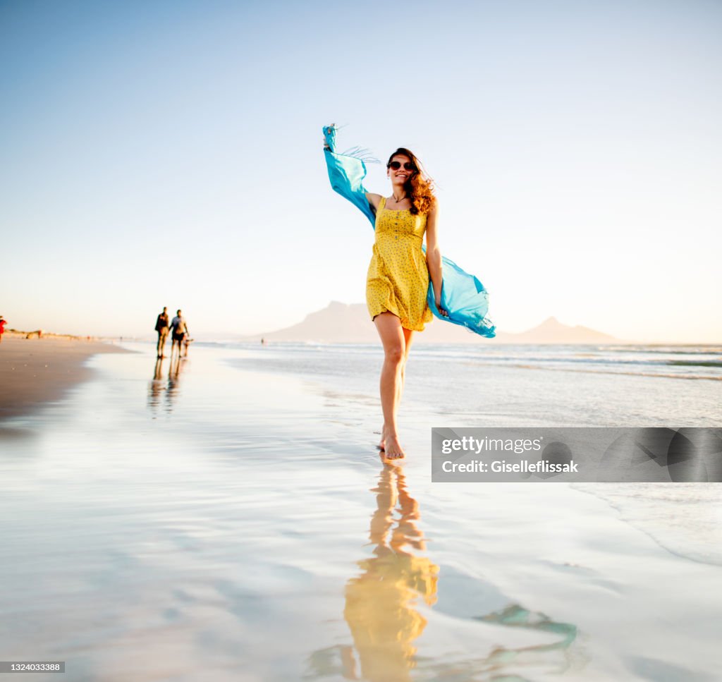 Carefree young woman walking along a beach with a scarf