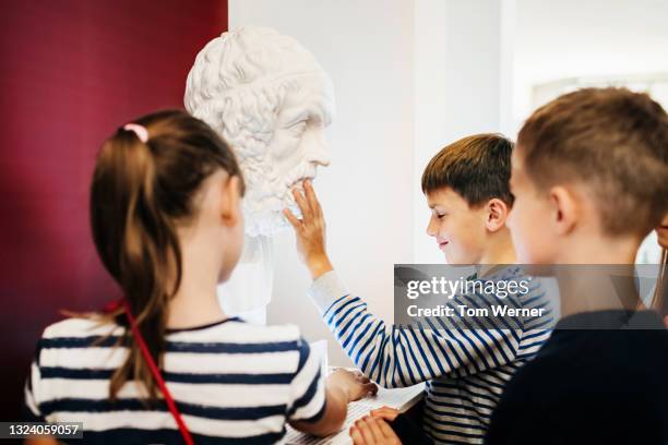 young boy touching bust on display in museum - bust museum stock-fotos und bilder