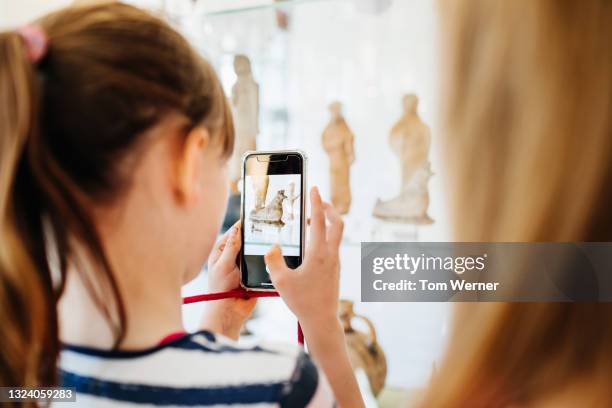 young girl taking photos of museum exhibit using smartrphone - museo fotografías e imágenes de stock