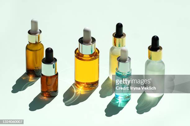 trendy beauty concept of facial serums, natural essential oil in cosmetic bottles with dropper and bright sunligth shadow on green mint turquoise background. - essential oil stock-fotos und bilder