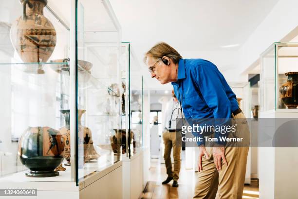 mature man listening to audio guide while exploring museum - museum visit stock pictures, royalty-free photos & images