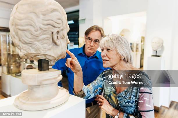 mature couple examining ancient bust on display in museum - bust museum imagens e fotografias de stock