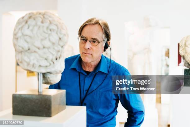 mature man looking at bust while listening to audio guide in museum - bust museum imagens e fotografias de stock