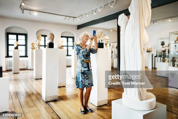mature woman taking pictures of sculptures in historical museum - art fair stockfoto's en -beelden