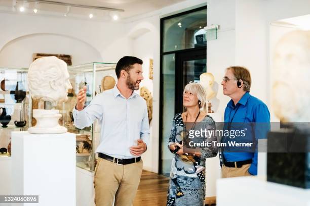 museum curator giving tour of classical exhibit to visitors - bust museum stock-fotos und bilder