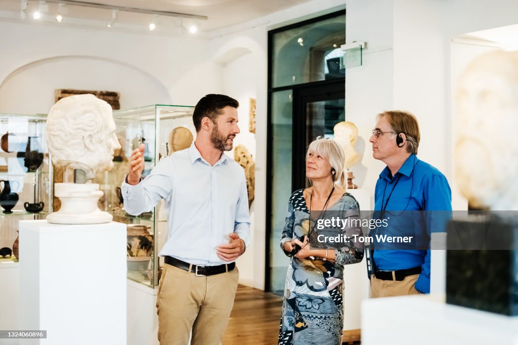 Museum Curator Giving Tour Of Classical Exhibit To Visitors