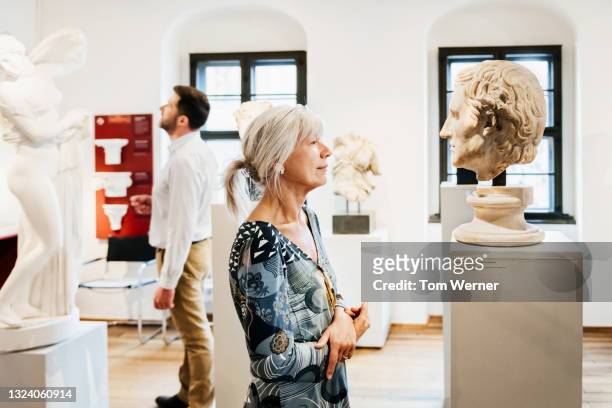 mature woman looking at sculpture in historical museum - bust museum stock-fotos und bilder