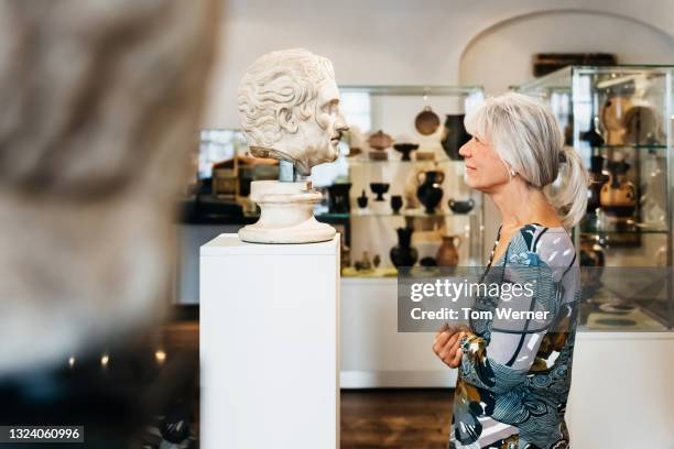 mature woman viewing classical busts in historical museum - bust museum imagens e fotografias de stock