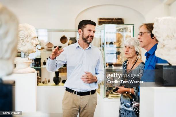 museum curator explaining exhibit to visitors - gids stockfoto's en -beelden