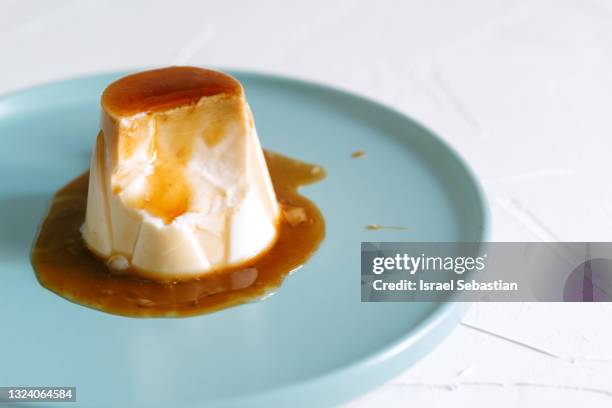 close up view of cheese pudding with delicious caramel on top with a piece missing because it has been eaten on a blue plate. - panna cotta photos et images de collection
